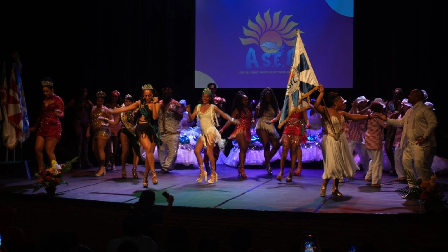 Apresentação coletiva no palco do Teatro Municipal com a bandeira da ASEC